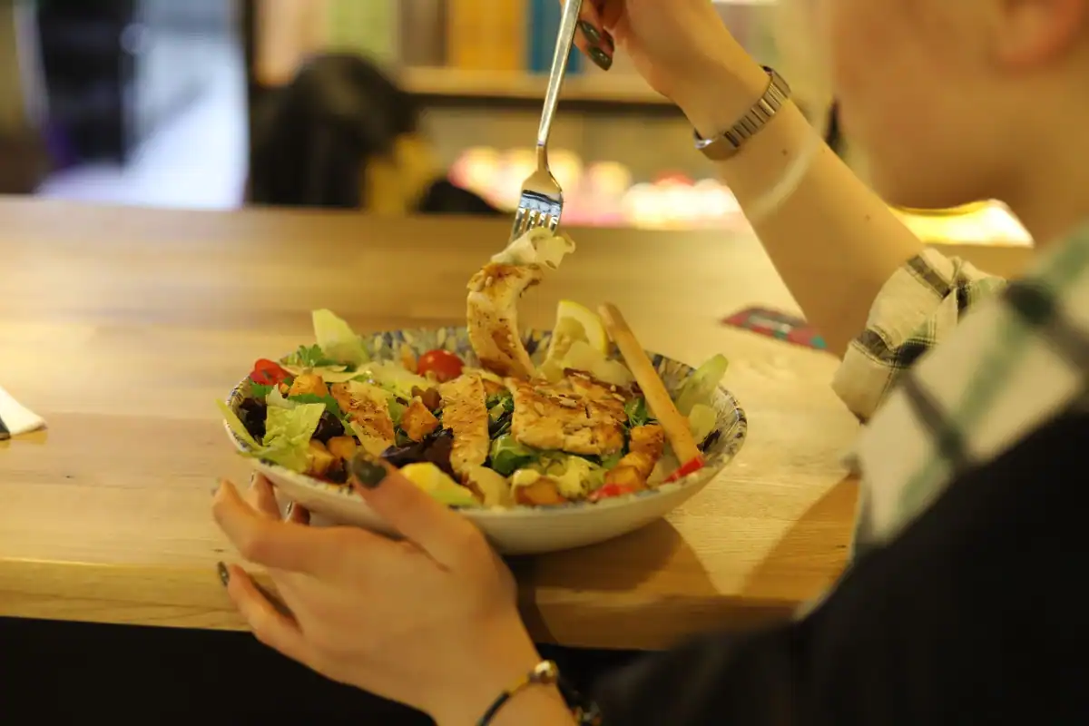 Femeie care mănâncă încet dintr-un bol cu salată de pui, la o masă de lemn