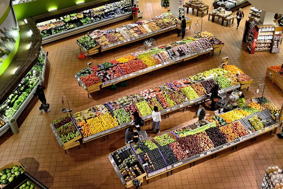 Raioane de legume și fructe într-un supermarket, văzute de sus, cu clienți