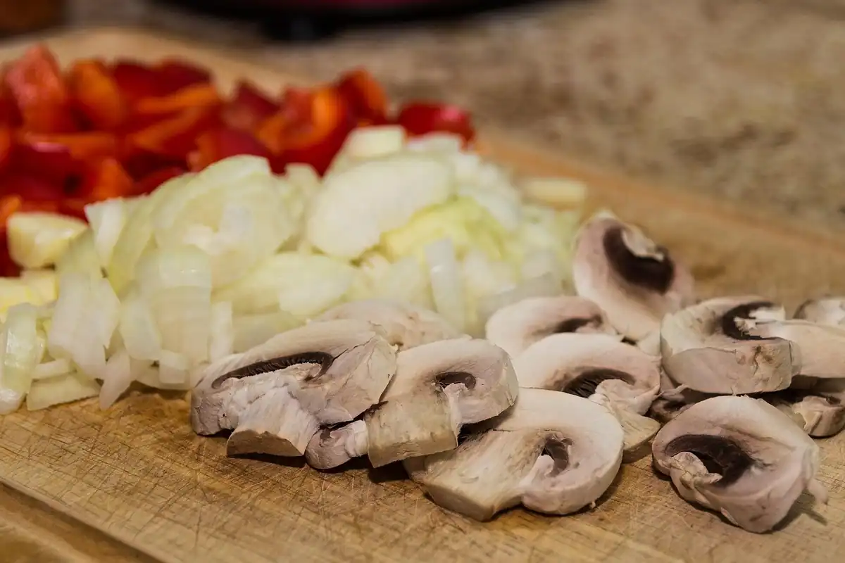 Ciuperci, ceapă și ardei tăiați bucăți pe o tocătoare, ingrediente pentru prânzul la birou